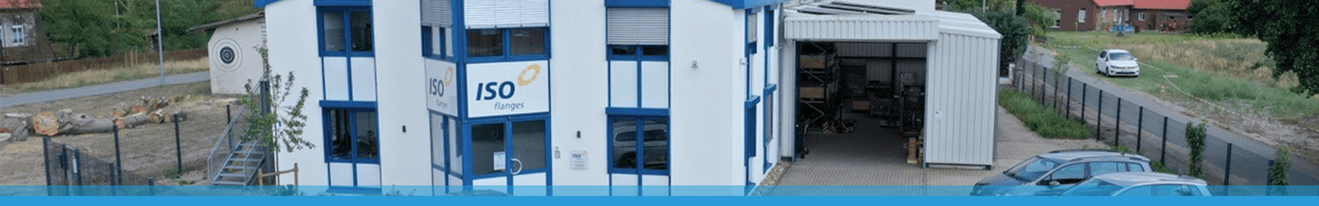 Weißes und blaues Industriegebäude mit ISO-Zeichen, Hersteller Isolierflansche, offener Garage und geparkten Autos.